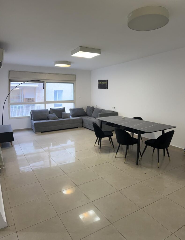 Modern minimalist living room with grey sofa and black dining table, bright space with large window.