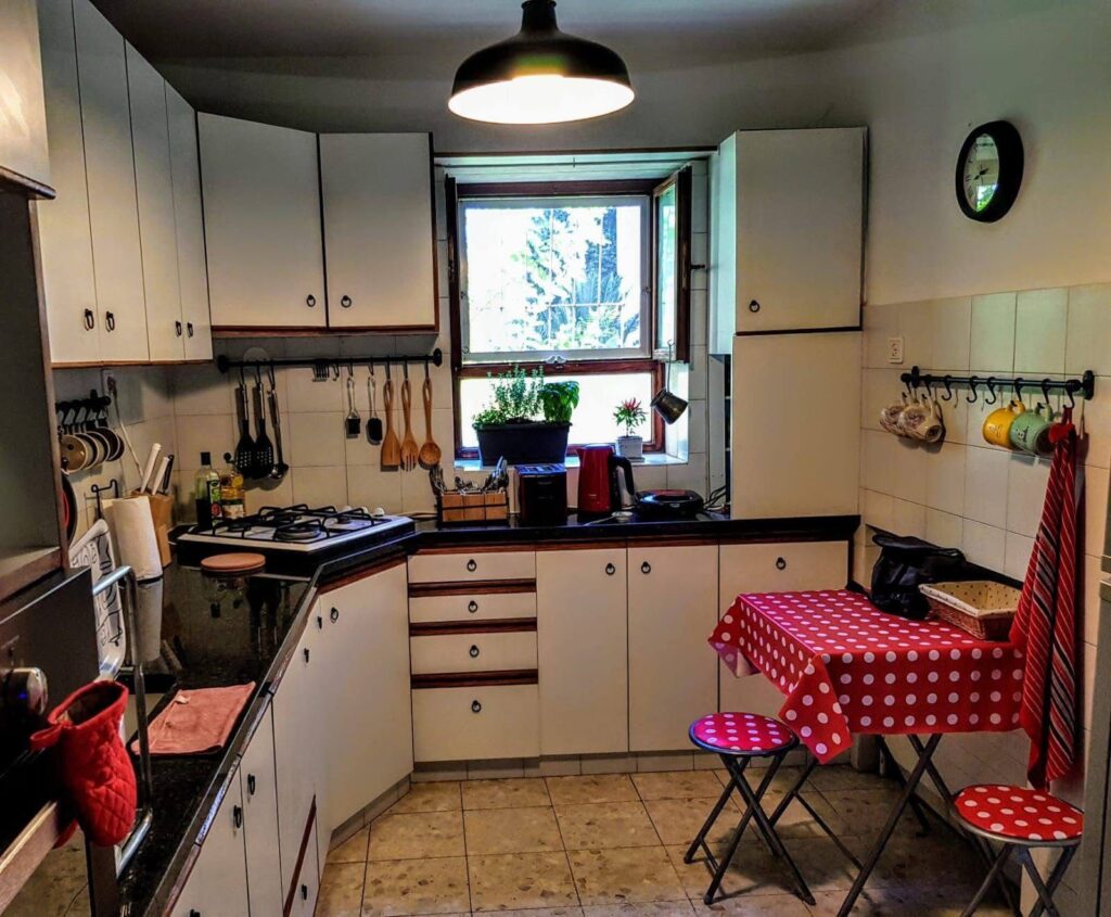 Cozy kitchen with white cabinets, black countertops, and a small dining area with red polka dot tablecloth. Bright window view.