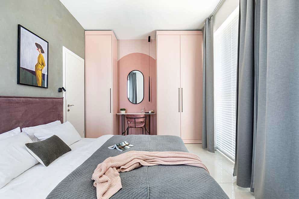 Modern bedroom with pink wardrobe and stylish decor, large window with gray curtains, and contemporary artwork.
