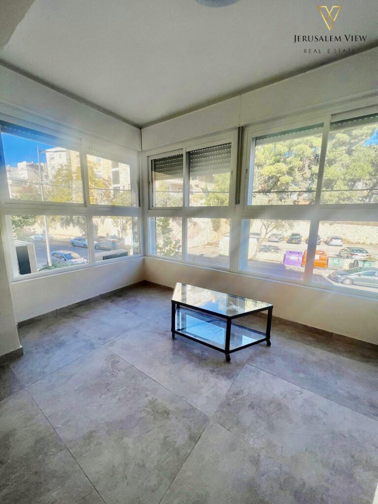 Bright sunlit corner room with large windows, modern tile flooring, and minimal decor.