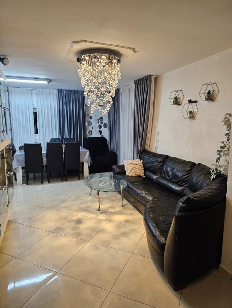 Elegant living room with black leather sofa and modern chandelier.