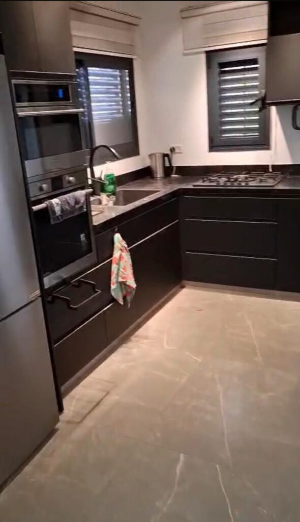 Modern black kitchen cabinets with built-in oven and stovetop, gray countertops, and windows with blinds.