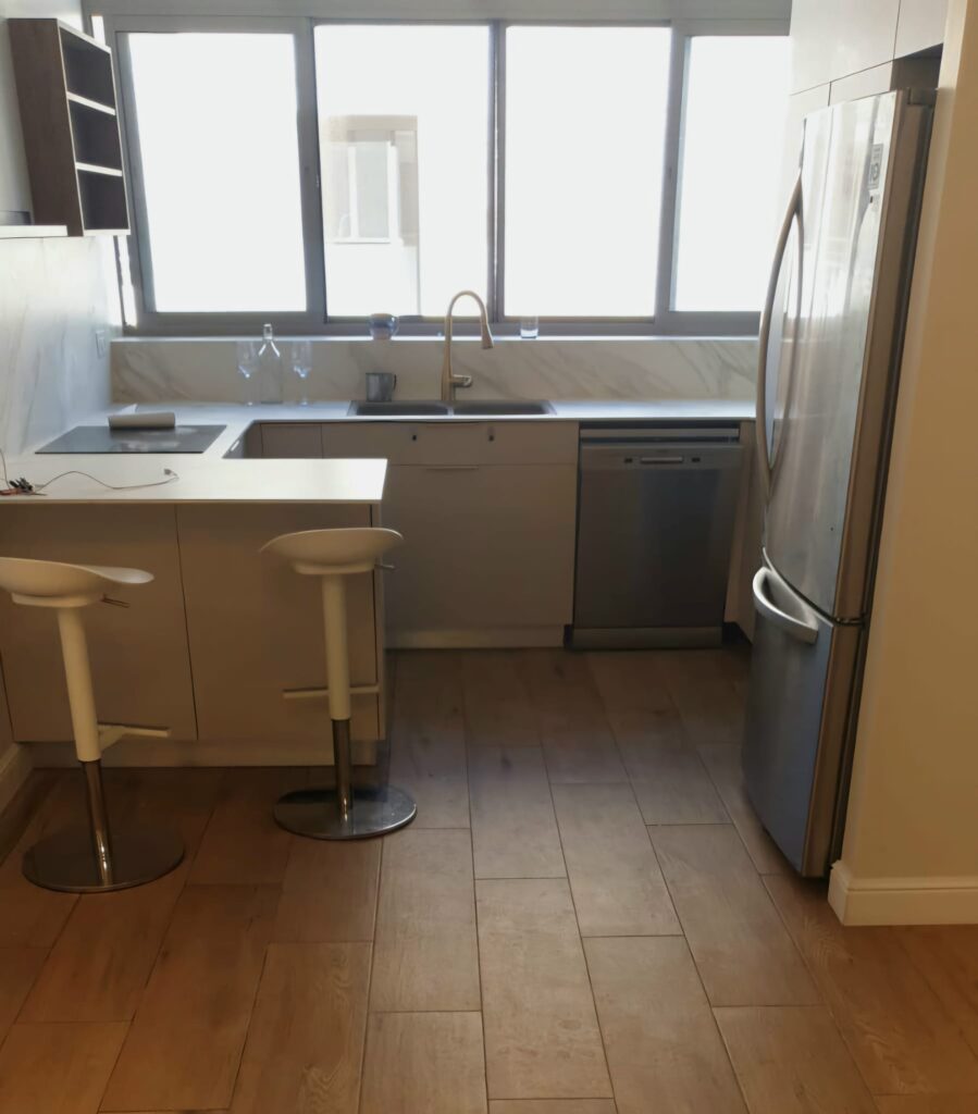 Modern kitchen with large window, stainless steel refrigerator, and beige cabinets.