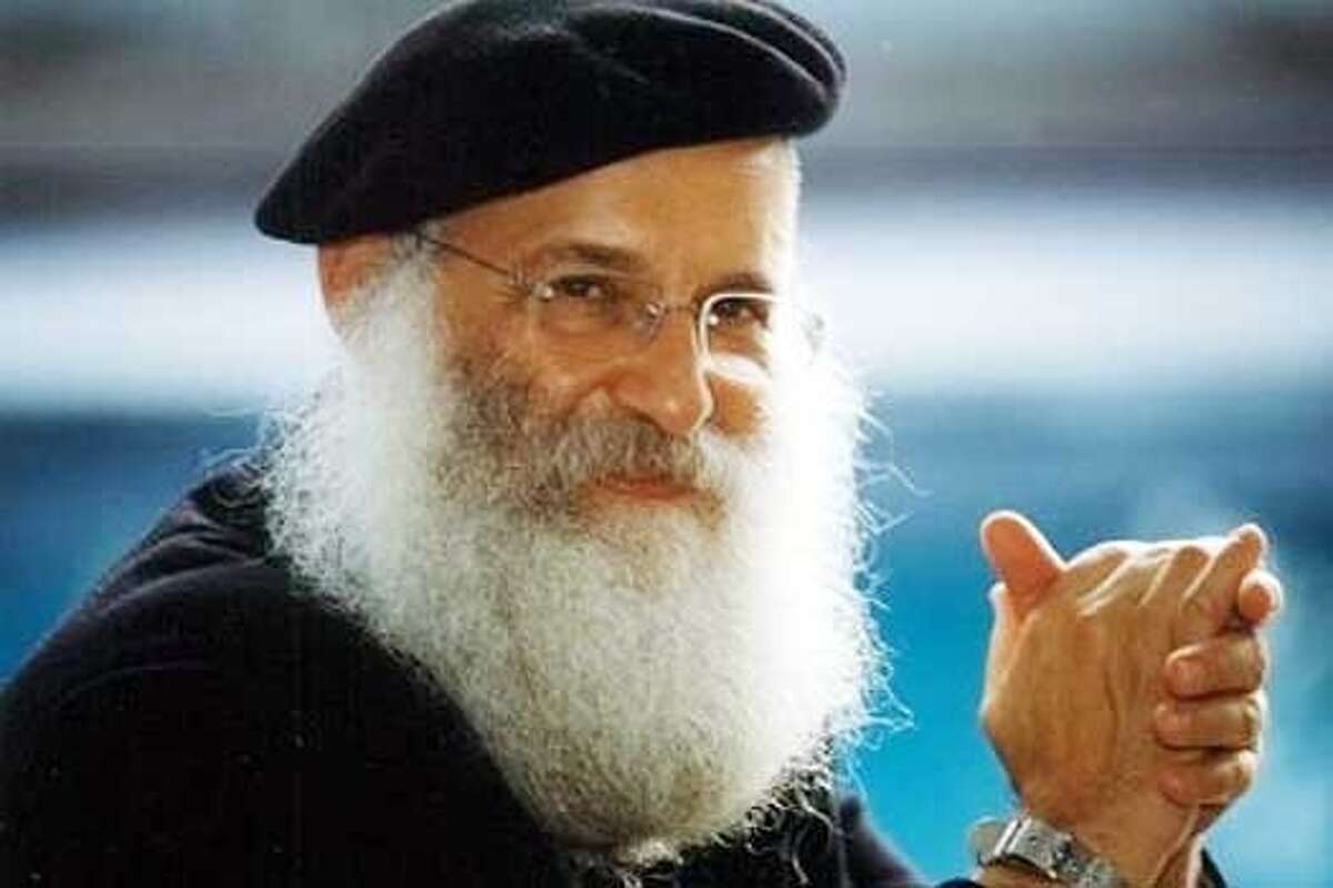 Elderly man with a white beard, glasses, and a black beret, smiling confidently, in a professional portrait.