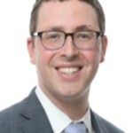 A professional man in glasses smiling in a business suit.