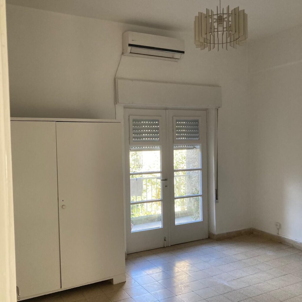 Bright room with white walls, glass door leading to balcony, air conditioning, and ceiling light fixture.