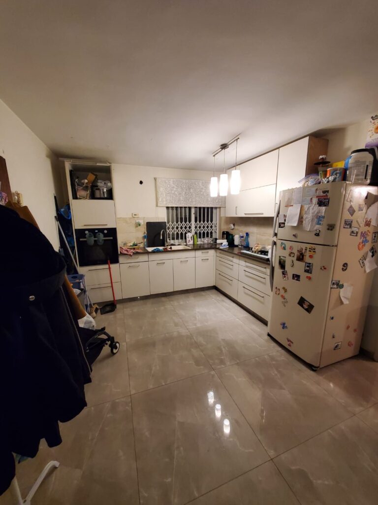 Modern kitchen with white cabinetry, refrigerator with magnets, and beige tiled floor in well-lit space.