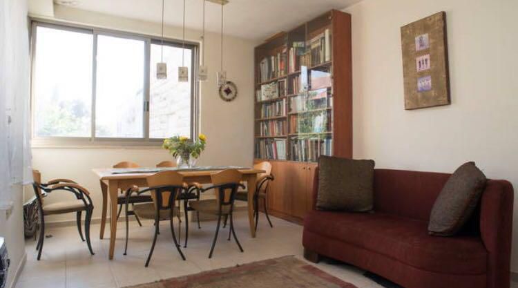 Vintage dining room with wooden table, chairs, bookshelf, and cozy red sofa in natural light.
