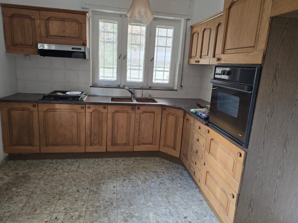 Wooden kitchen cabinets and countertop with a double sink, oven, and window in a cozy home kitchen.