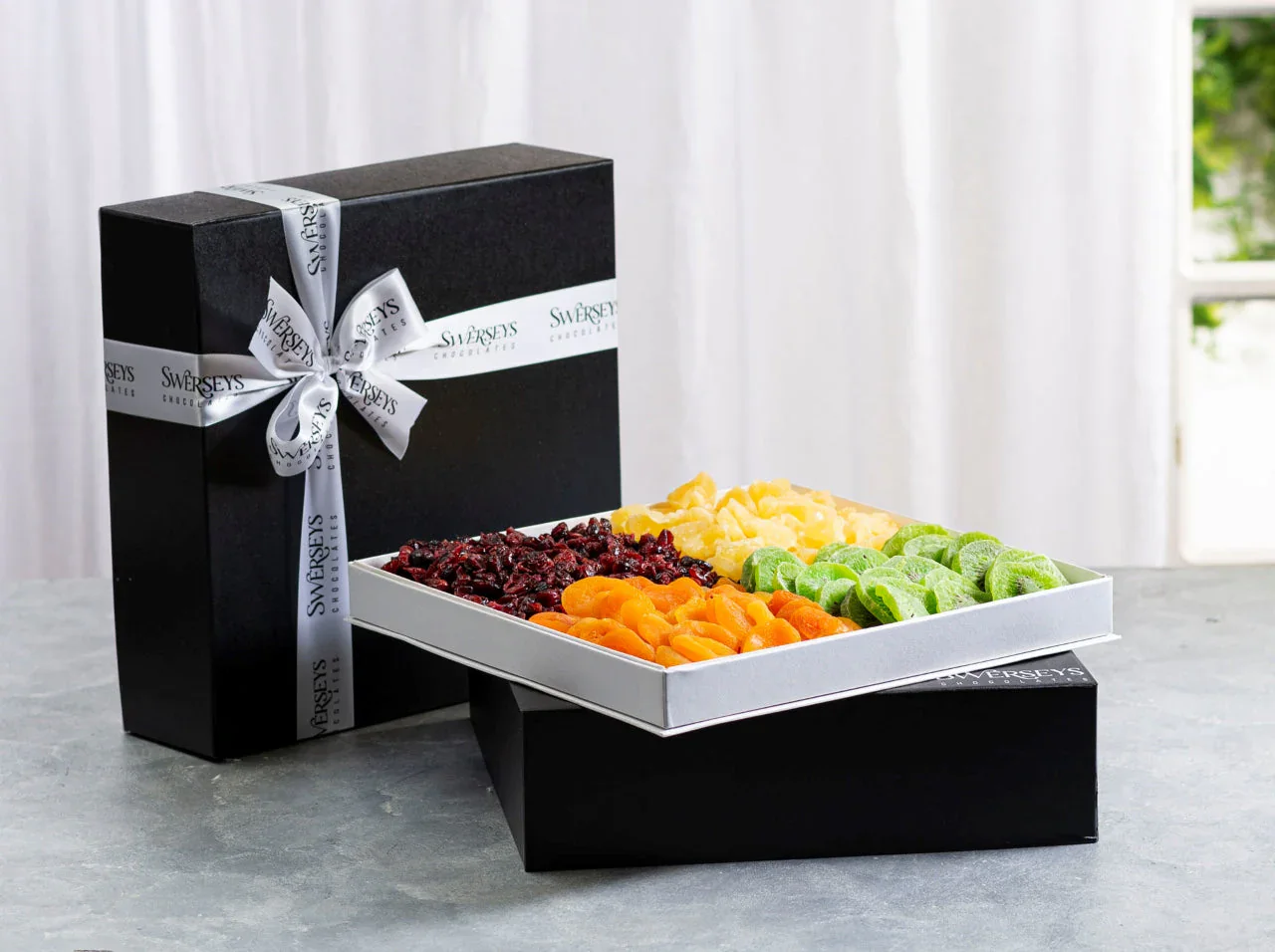 Assorted colorful gummy candies in a white box with a black gift box on a gray surface.