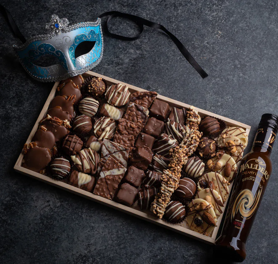 Rich assorted chocolates and truffles in a wooden box, with a Venetian mask and a bottle of whisky.