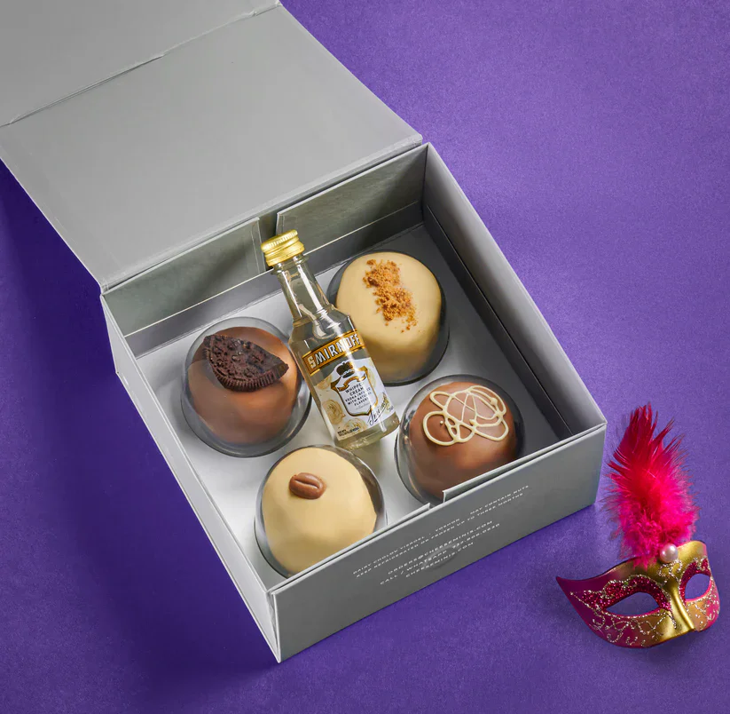 Miniature gourmet chocolates and a tiny liquor bottle in a stylish gift box on purple background.