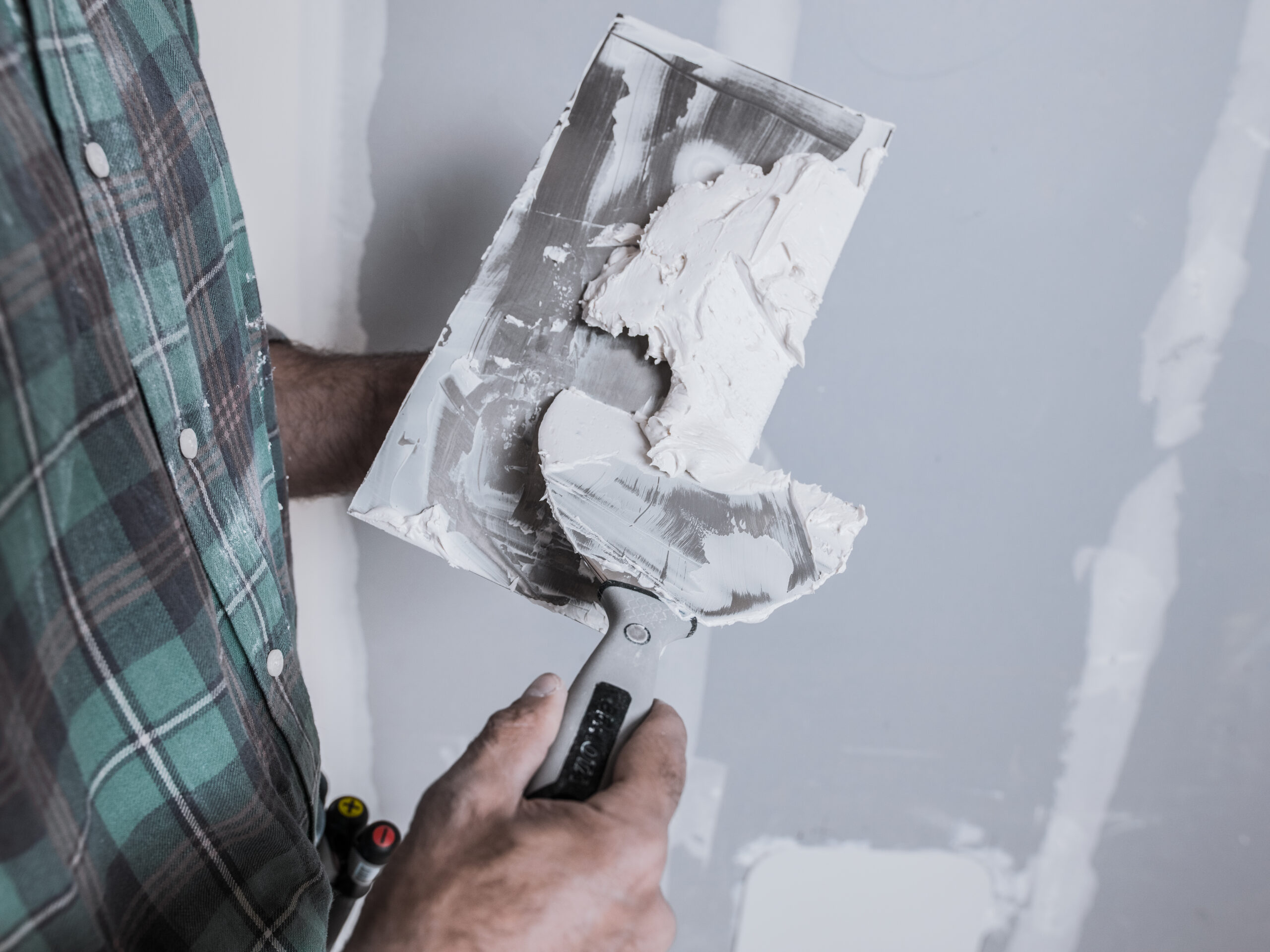 White wall plaster being smoothed with a putty knife during drywall installation or repair.