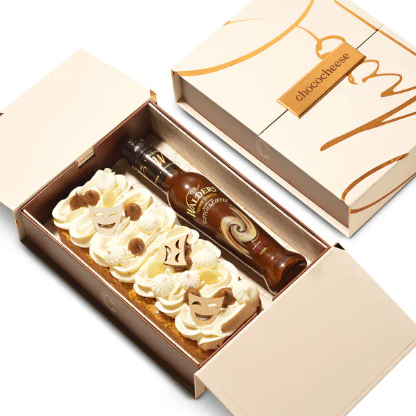Delicious cheesecake slices decorated with chocolate and a whiskey bottle in a gift box.