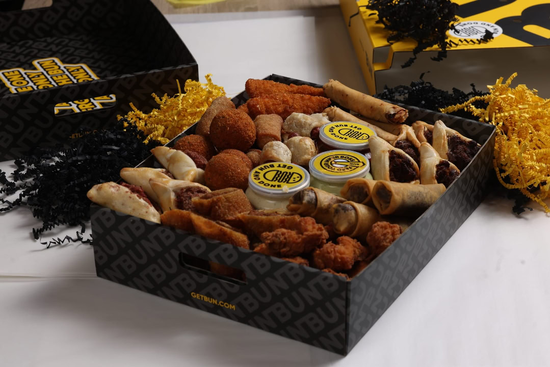 Assorted chicken wings, fried snacks, and dipping sauces in a black box. Perfect for parties and gat.