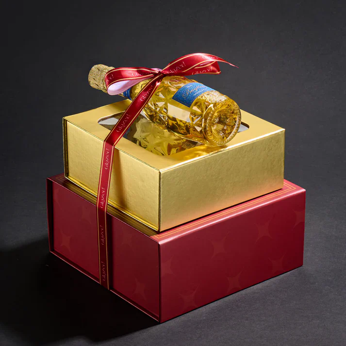 Golden gift box with champagne bottle and red ribbon for celebration.