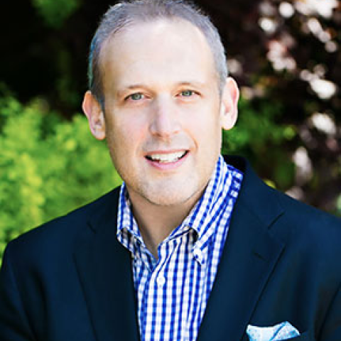 Business professional smiling outdoors with greenery background.