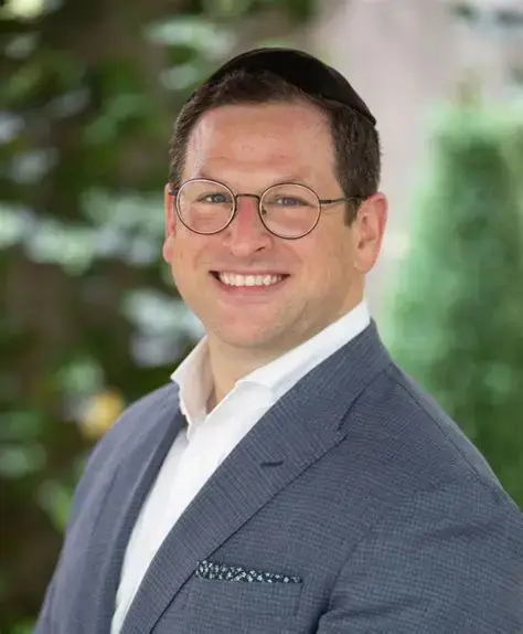 Business professional portrait of a smiling man in a suit with glasses outdoors.