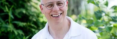 A smiling man wearing glasses outdoors in a lush green garden.