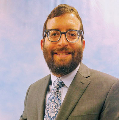 Professional man in a suit with glasses smiling at the camera at a conference or event.